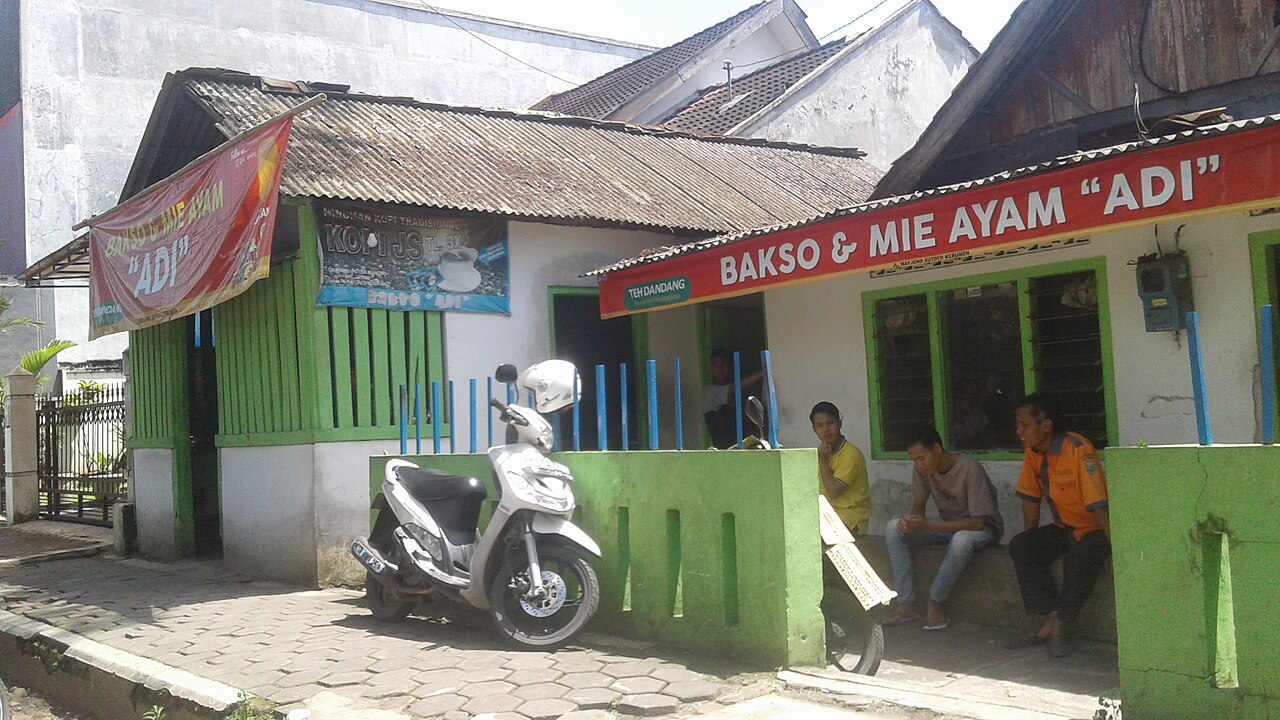 Warung bakso dan mie ayam bercat hijau dengan papan nama merah, beberapa orang duduk di depannya